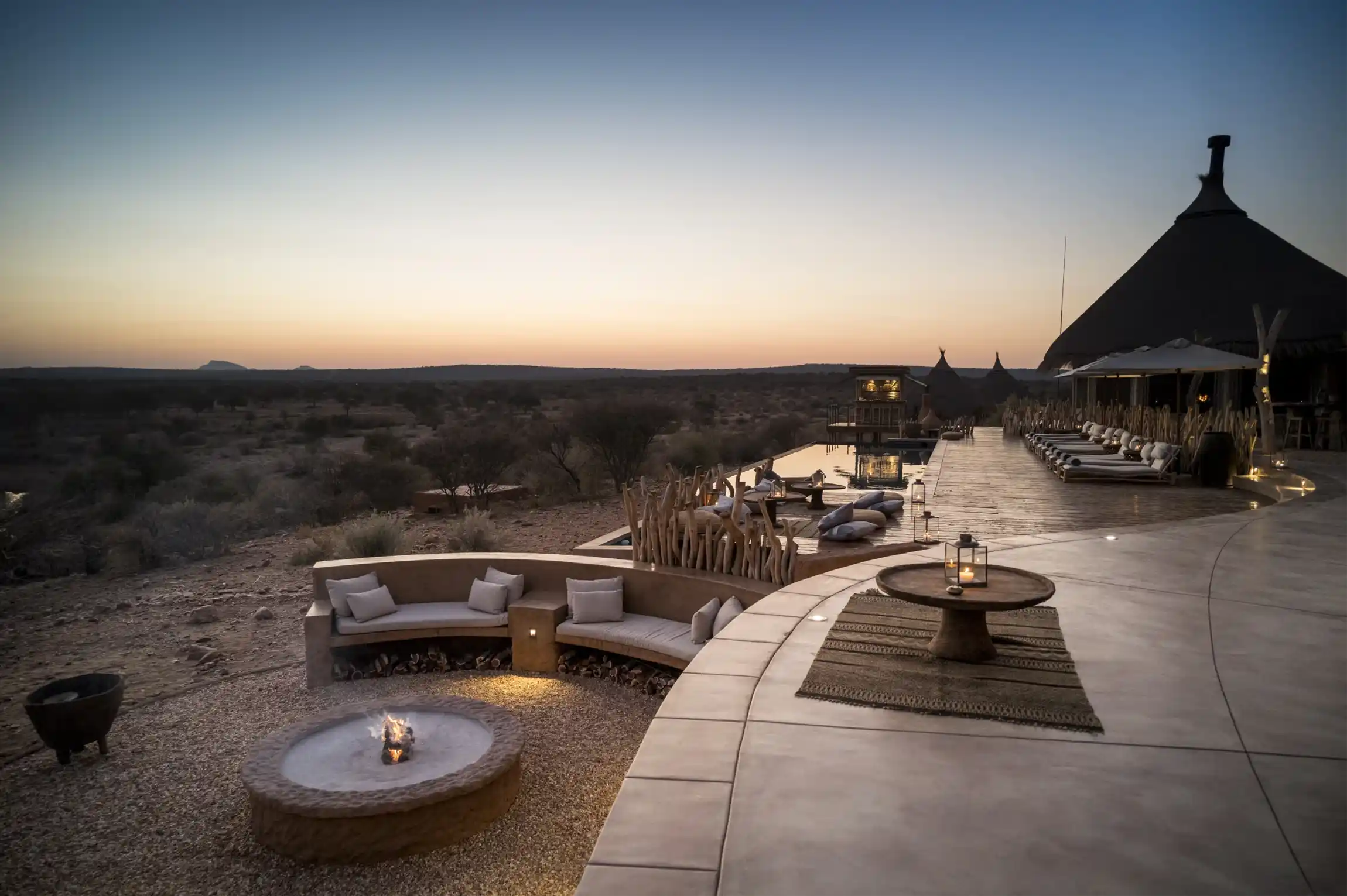 Zannier Omaanda, Namibia. Pool area and boma fireplace overlooking the savannah at sunset.